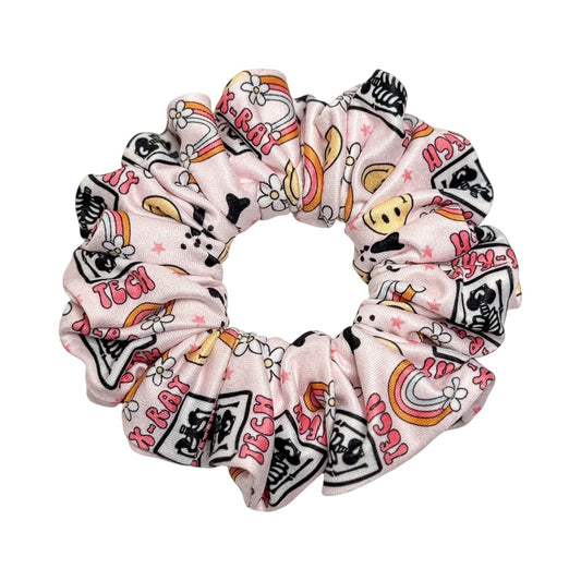 Headband Studio pink scrunchie with medical tech print, featuring X-ray images, rainbows, and flowers. Handmade from soft polyester.
