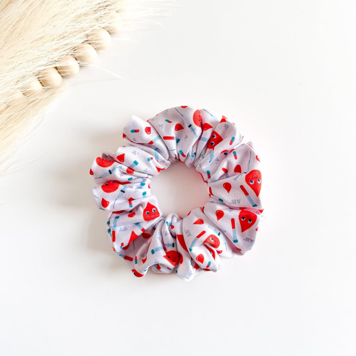 Headband Studio white scrunchie with red blood drop characters, syringes, and tubes print. Handmade hair accessory.