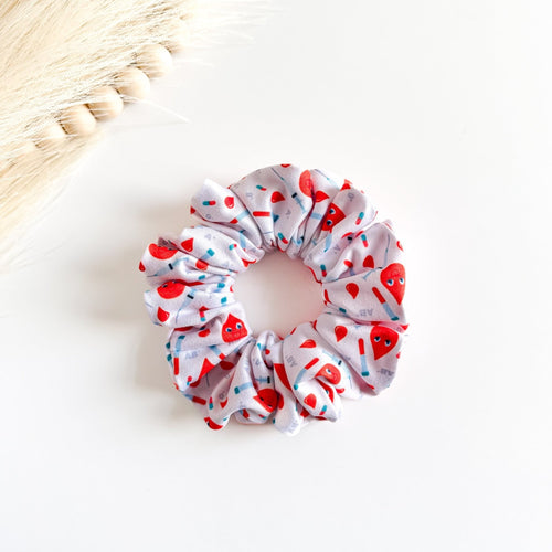 Headband Studio white scrunchie with red blood drop characters, syringes, and tubes print. Handmade hair accessory.