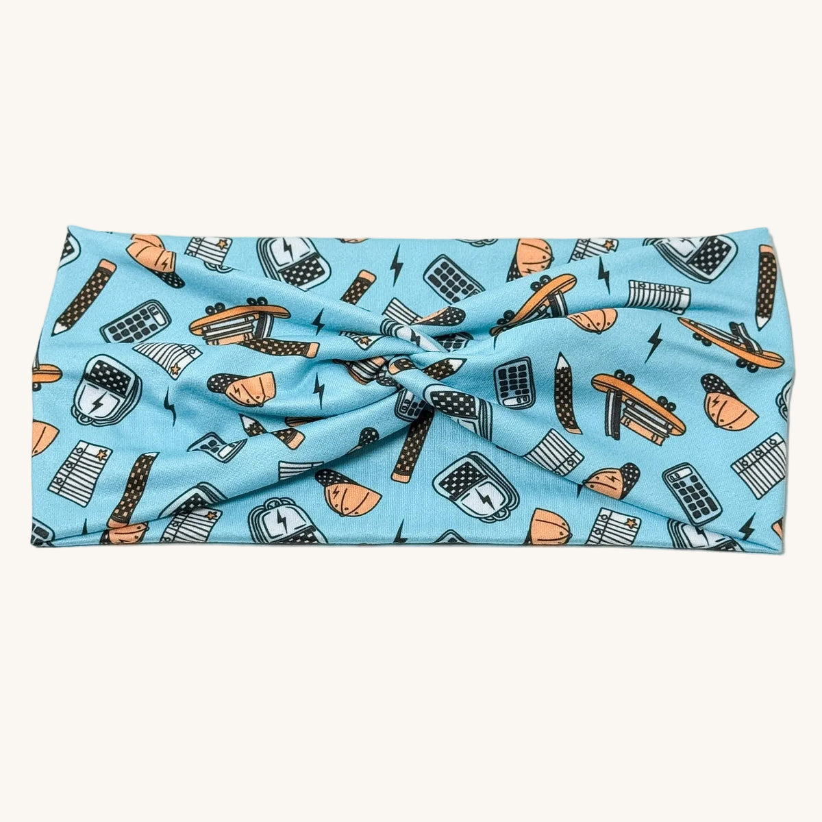 A light blue knotted headband featuring a pattern of school supplies like pencils, rulers, and books in orange, black, and white, displayed flat against a white background.