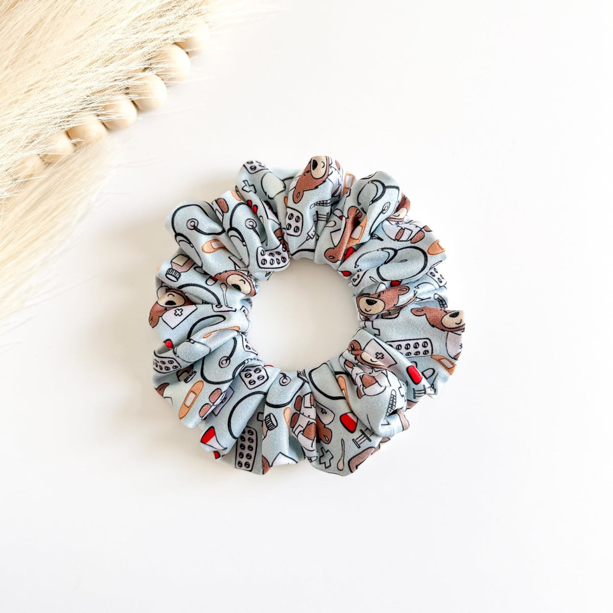 Headband Studio light blue scrunchie with a pattern of medical icons like stethoscopes, band-aids, pills, and teddy bears in nurse outfits.