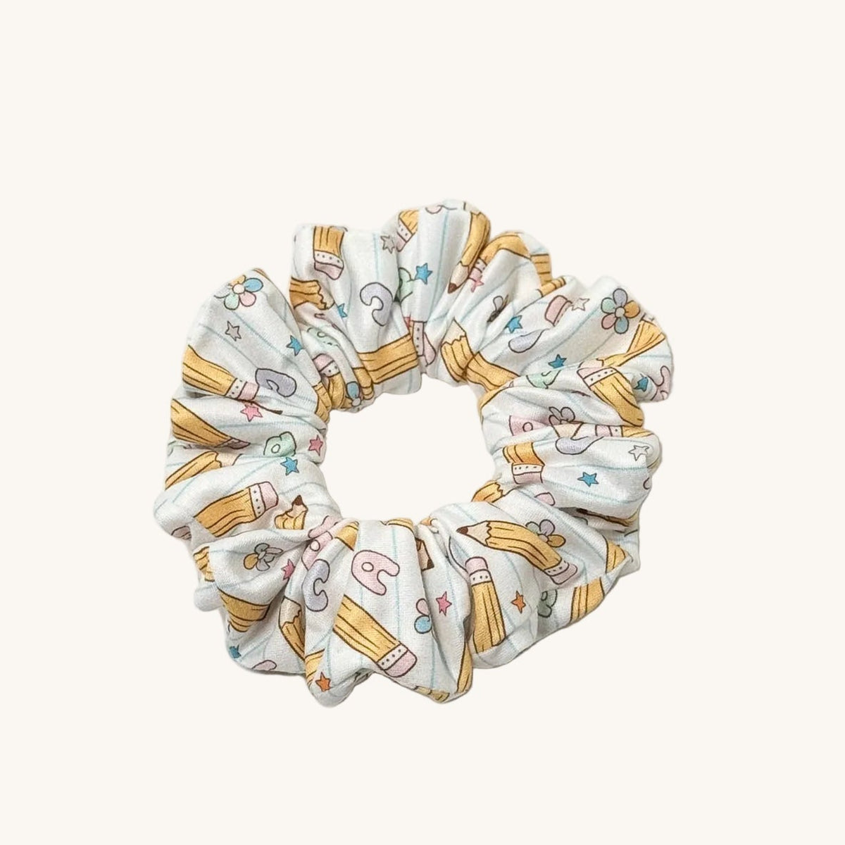 A fabric scrunchie with a white background and a yellow pencil pattern, shown on a plain white surface.