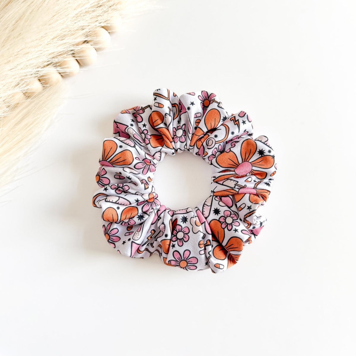 Headband Studio white scrunchie with pink and orange medical-themed print, including flowers, stethoscopes, and syringes.