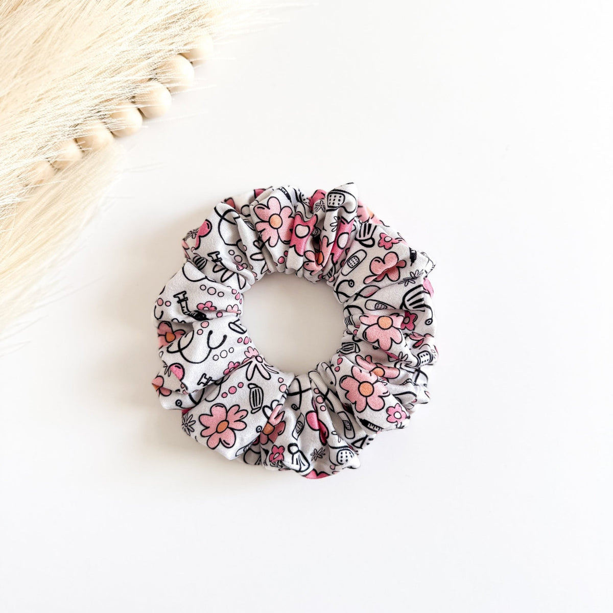 white scrunchie with pink flowers and medical icons like stethoscopes and masks.