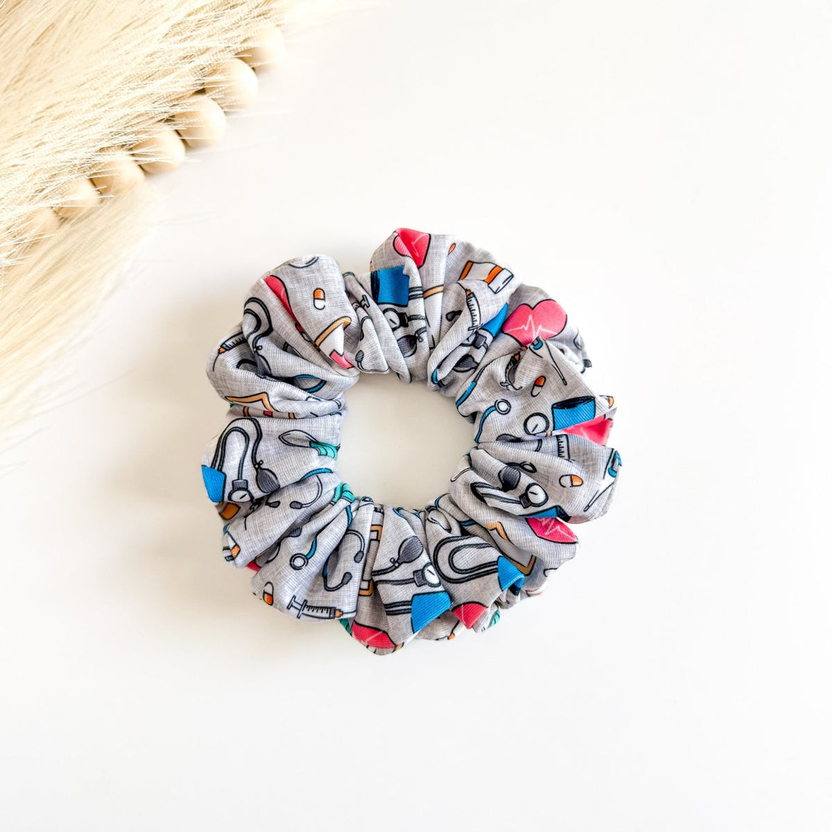 Headband Studio grey scrunchie with colorful medical icons like stethoscopes, heartbeats, and tools. 