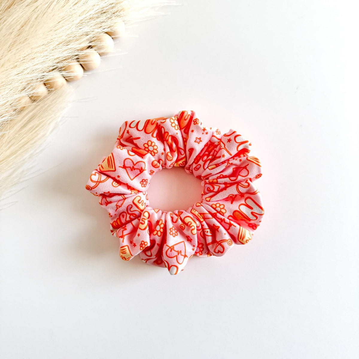 Headband Studio pink scrunchie with orange medical icons like stethoscopes, syringes, and pills.