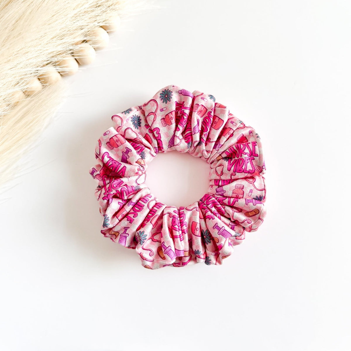 Headband Studio pink scrunchie with nurse vibes print, featuring band-aids, syringes, and flowers. 