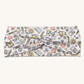 A fabric headband with a twisted center, featuring a colorful doodle-style pattern of school supplies, flowers, and hearts on a white background.