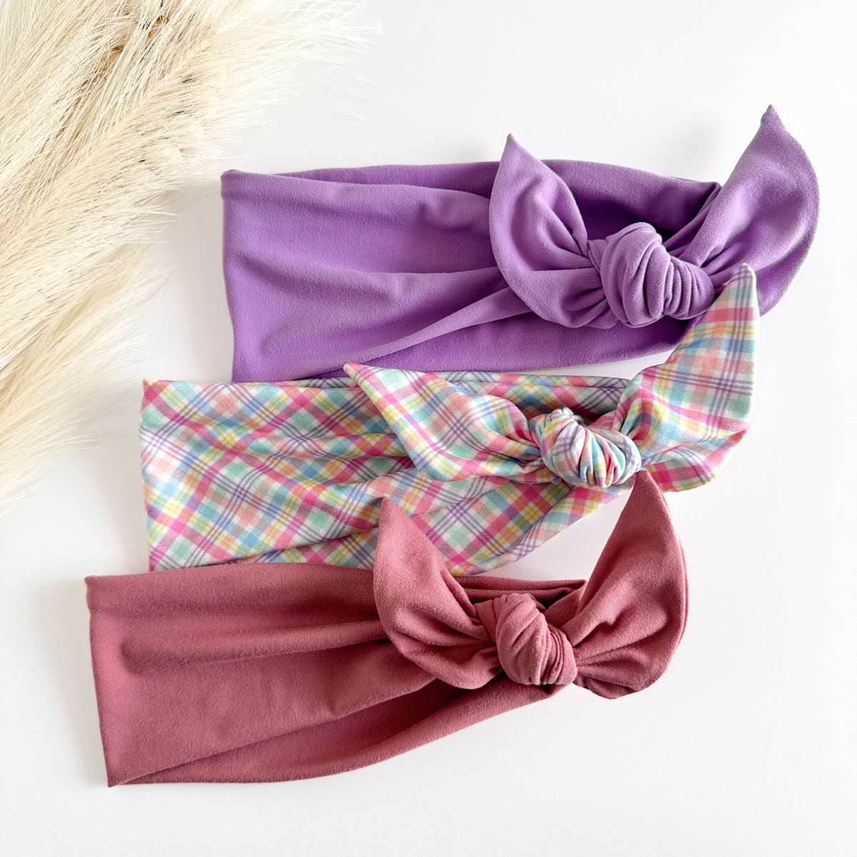 Headband Studio three soft fabric headbands in purple, pastel plaid, and rose pink with adjustable tie knots.