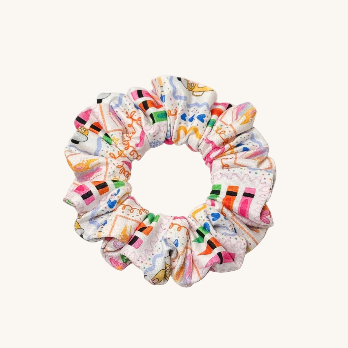 A fabric scrunchie with a colorful retro graphic print on a white background, photographed on a clean light gray studio surface.