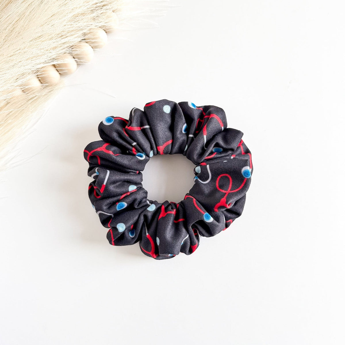 Headband Studio black scrunchie with red and blue stethoscope print, made of soft fabric for healthcare professionals.