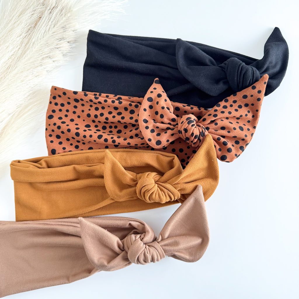 Headband Studio adjustable tie headbands in black, rust dalmatian print, mustard, and tan. Soft fabric with knotted detail.