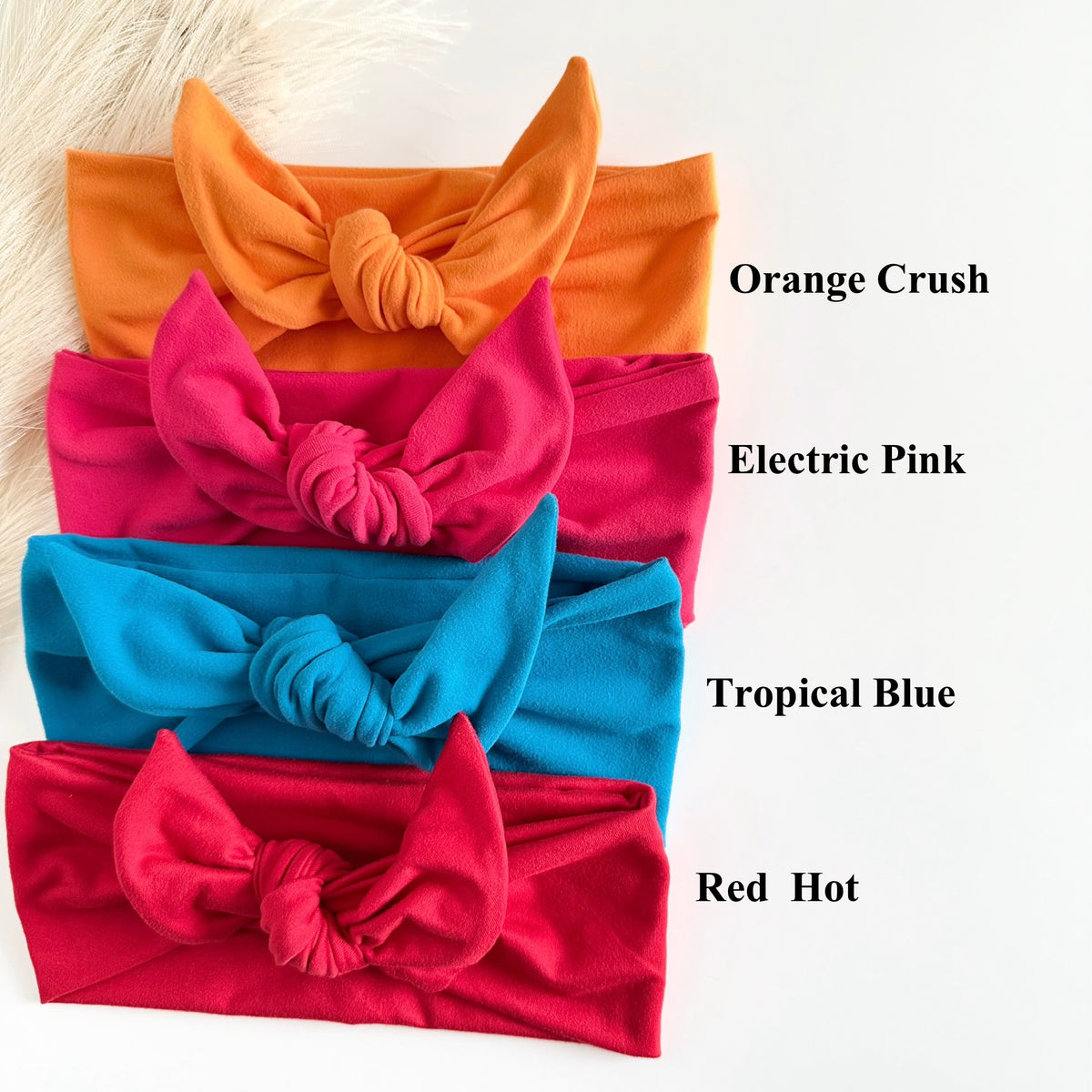 Four colorful headbands in Orange Crush, Electric Pink, Tropical Blue, and Red Hot on a white background.