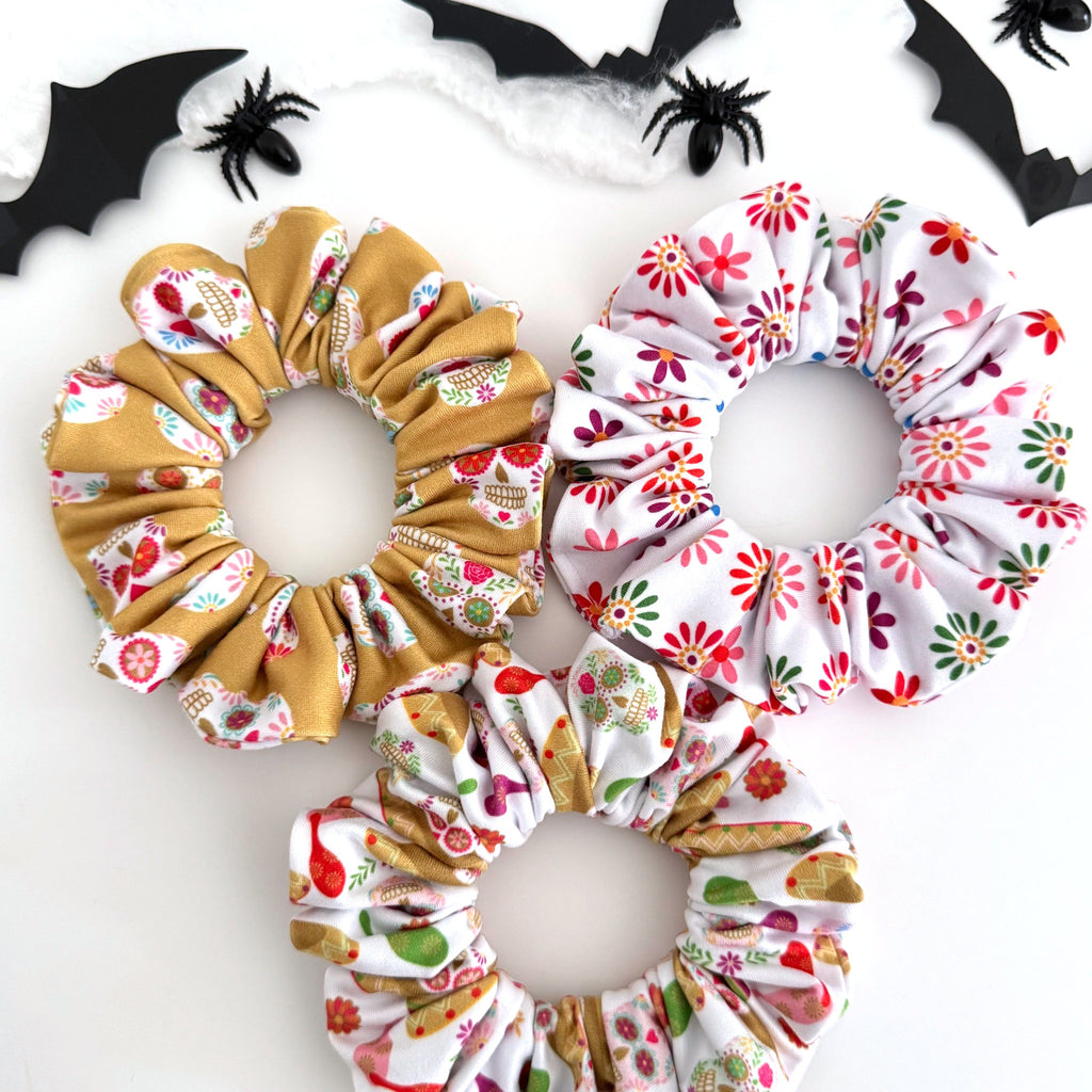 Three Day of the Dead scrunchies in sugar skull, sombrero and colorful flower prints with Halloween bats and spiders