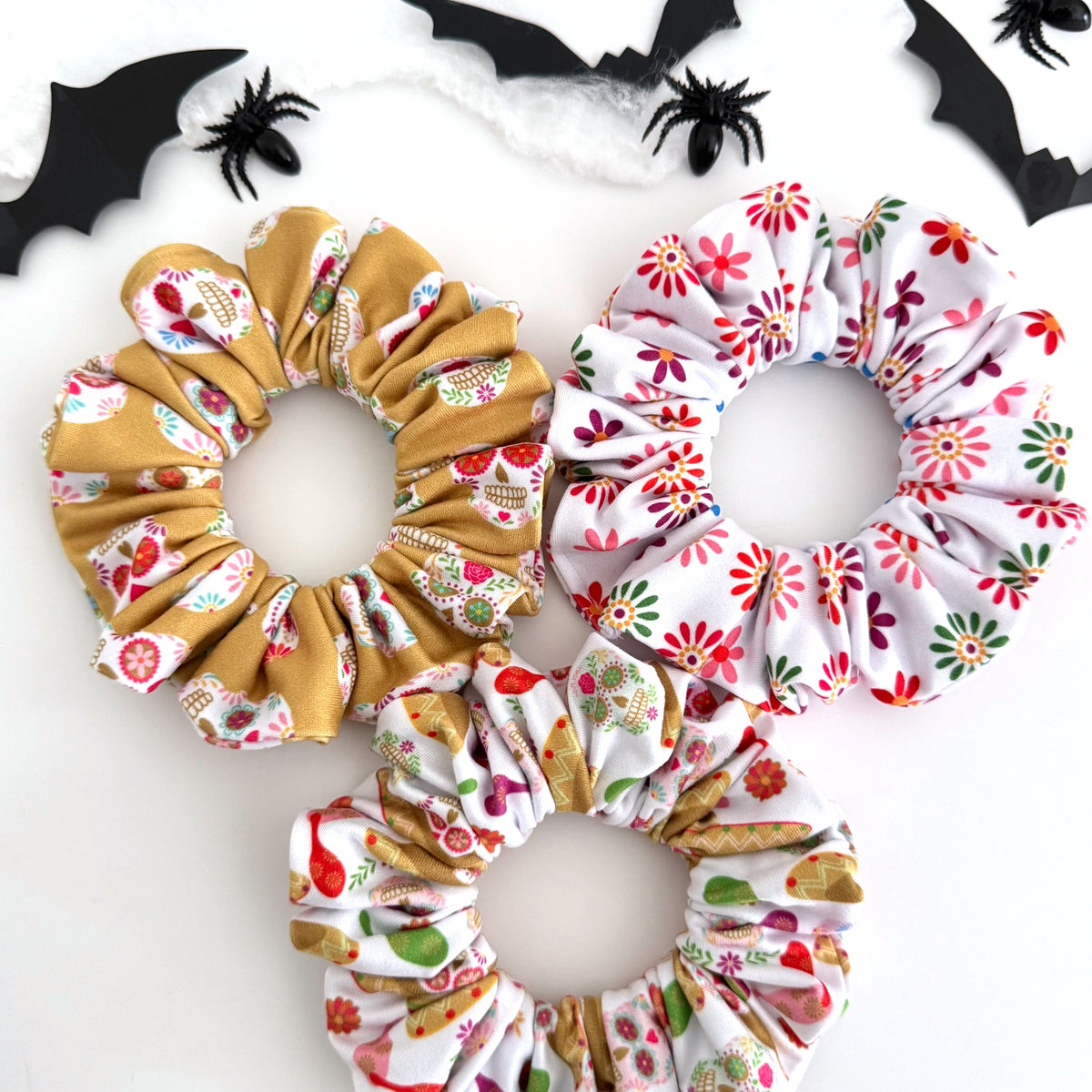 Three Day of the Dead scrunchies in sugar skull, sombrero and colorful flower prints with Halloween bats and spiders