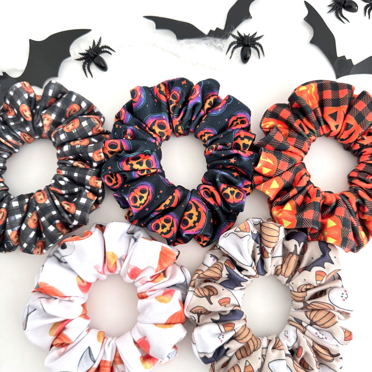 Pumpkin Halloween scrunchies in gingham, jack-o'-lantern, plaid and ghost prints with paper bats and spiders