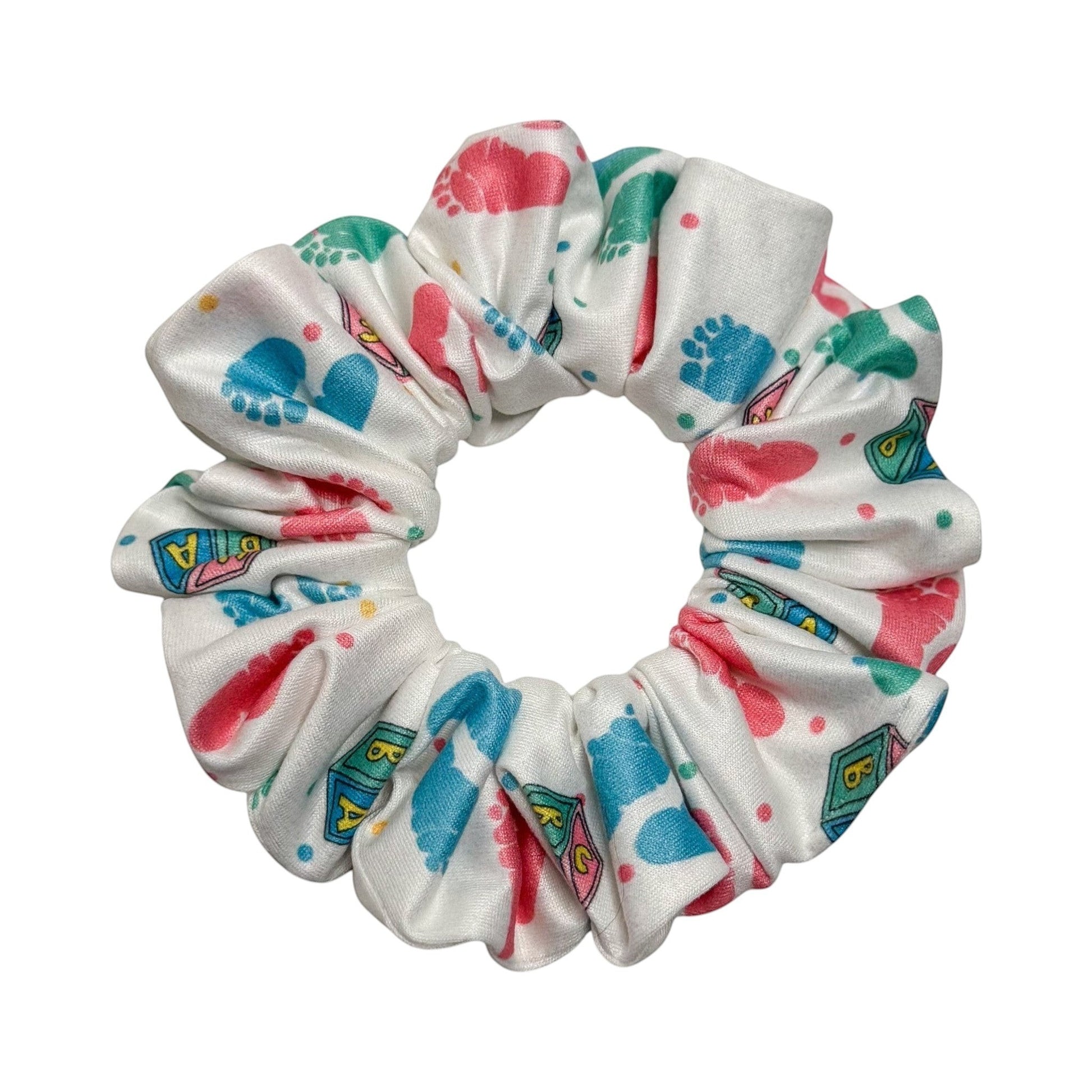 Headband Studio white scrunchie with pink, blue, and green baby footprints and blocks pattern. Handmade polyester.
