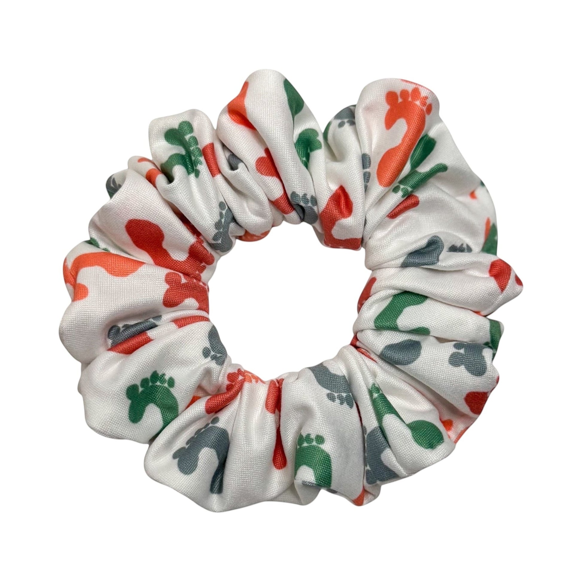 Headband Studio white scrunchie with a pattern of red, green, and grey footprints. Made from soft polyester.