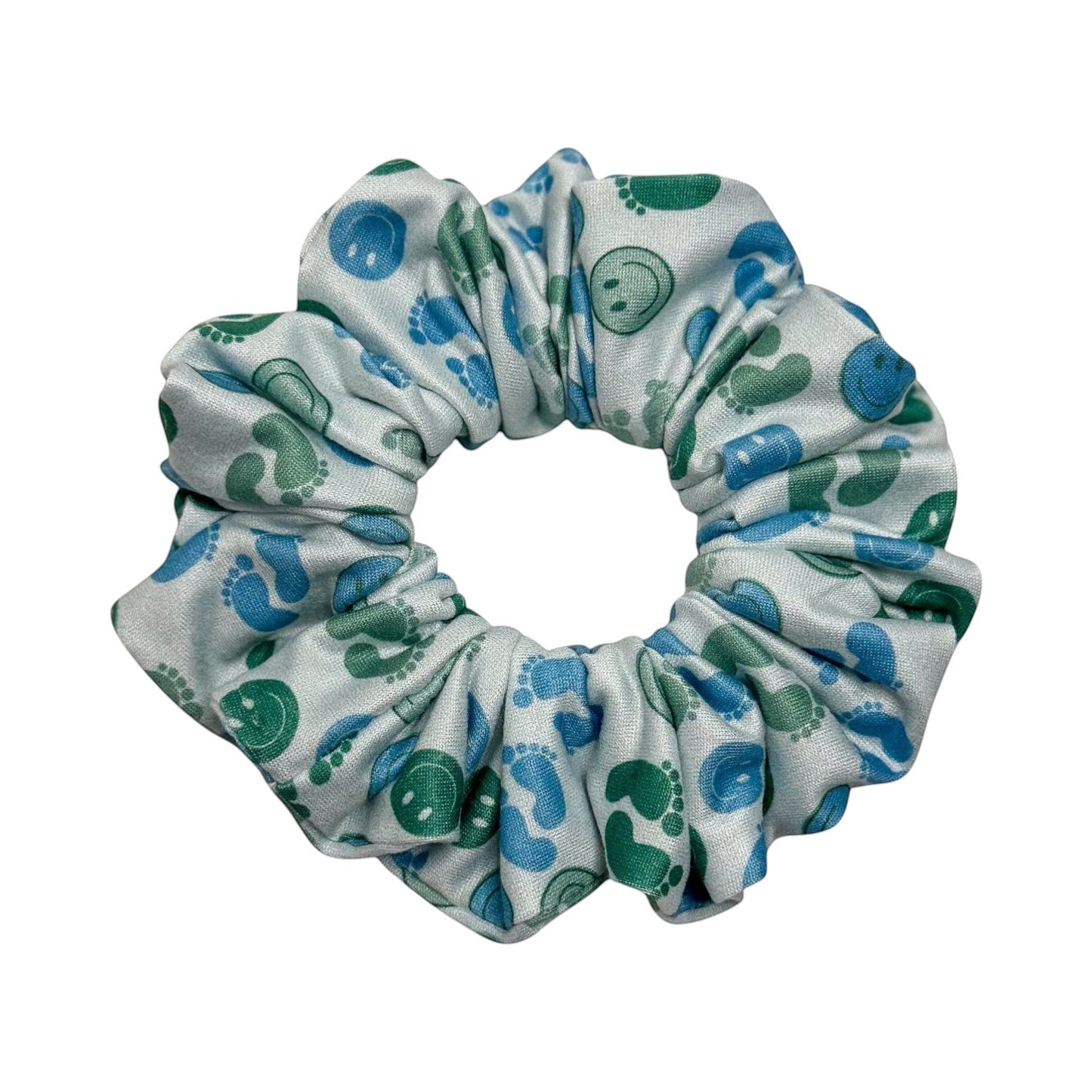 Headband Studio scrunchie with a white background featuring a pattern of blue footprints and green smiley faces. Made from soft polyester.