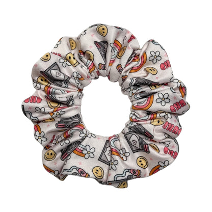 Headband Studio white scrunchie with a playful print of smiling faces, rainbows, and medical icons like stethoscopes and EKG lines.