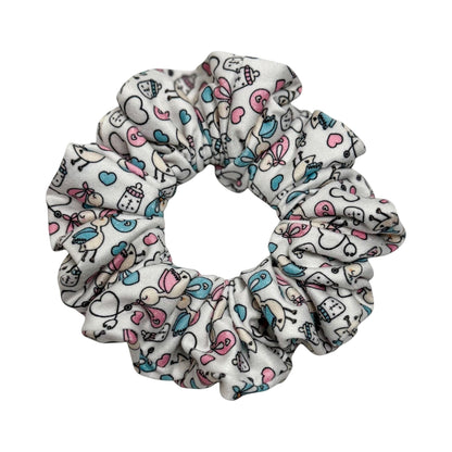 Headband Studio white scrunchie with a playful medical print featuring baby bottles, hearts, and birds in pink and blue.