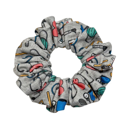 Headband Studio grey scrunchie with colorful medical icons like stethoscopes, heartbeats, and tools. Made of soft polyester.