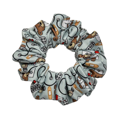 Headband Studio light blue scrunchie with a pattern of medical icons like stethoscopes, band-aids, pills, and teddy bears in nurse outfits.